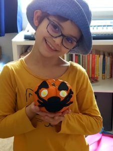 Child holding a mini-pumpkin decorated as a cat with a facemask
